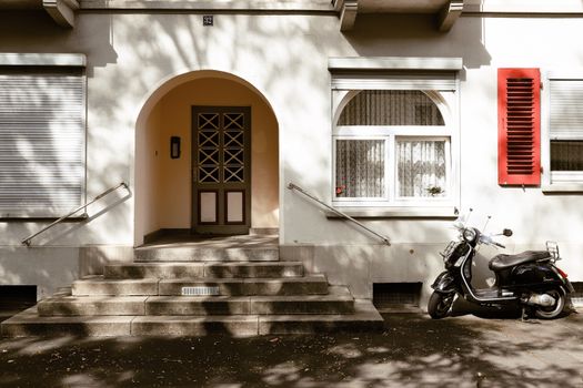 A charming urban scene in Kassel, Germany featuring a moped parked near a classic residential entrance with arched doorway.