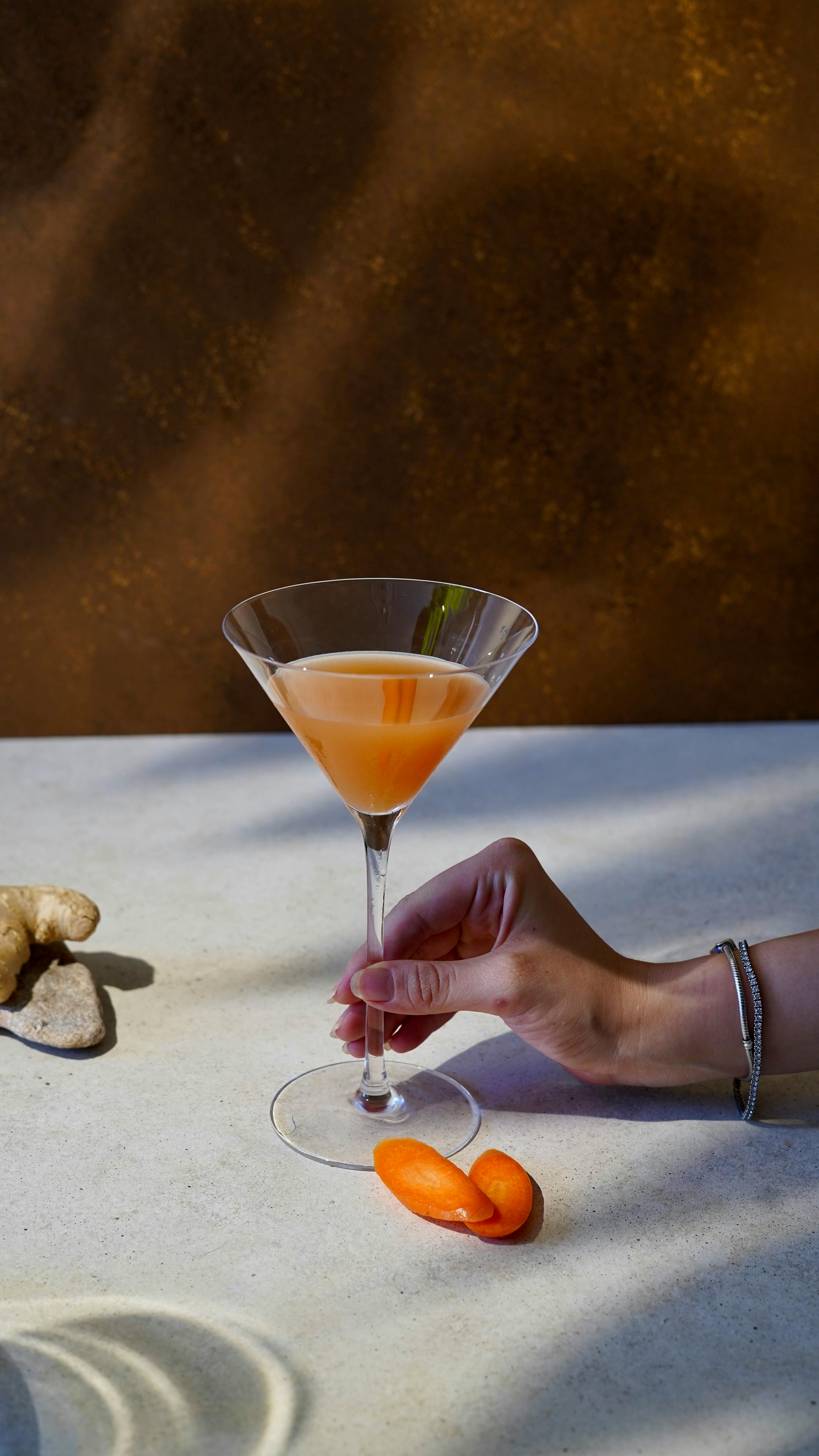 Stylish martini glass with cocktail, hand, and citrus garnish on a modern table.
