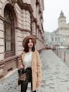 一位戴着帽子、穿着外套的时尚女士漫步在拥有经典建筑的城市街道上