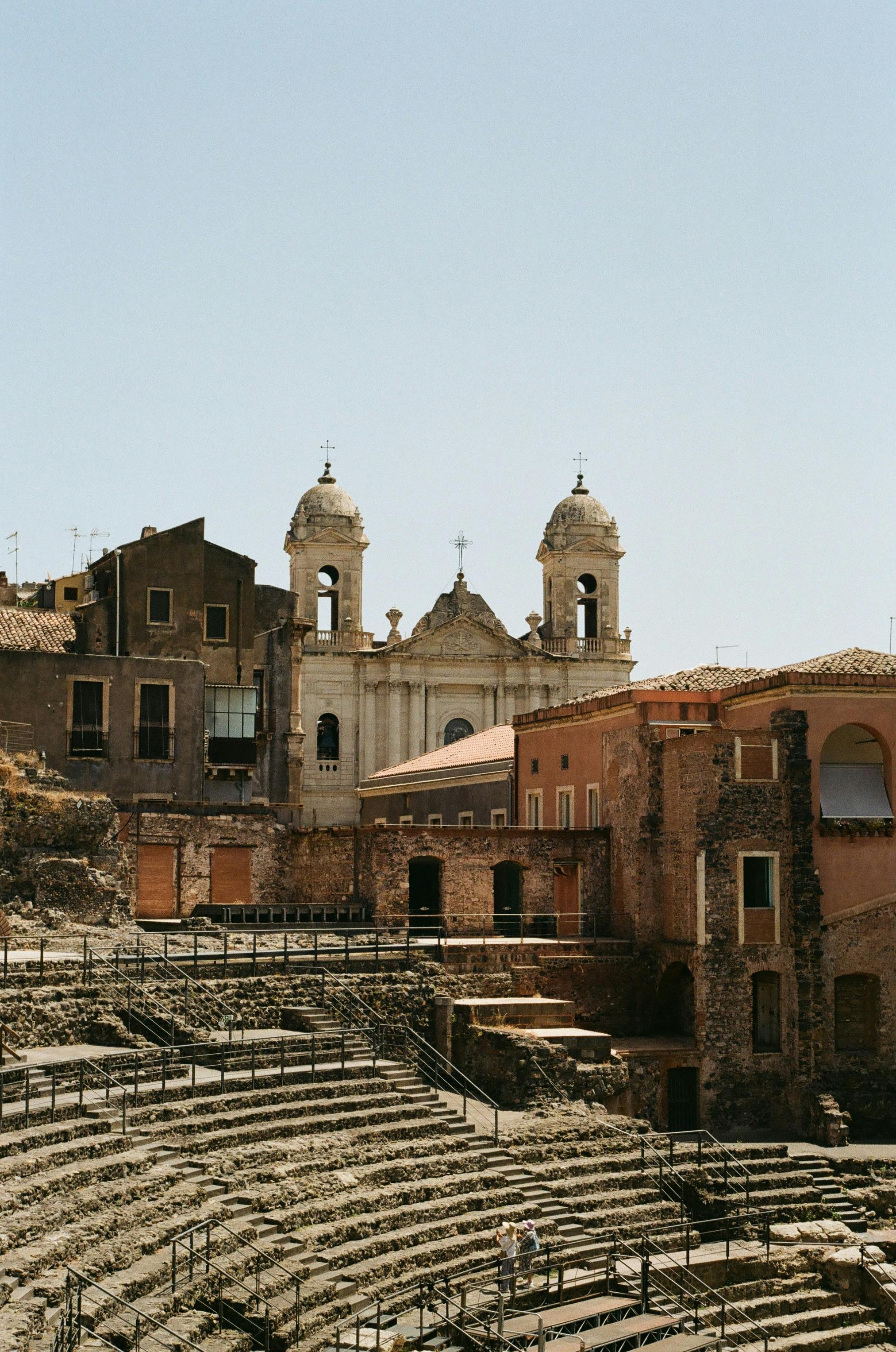 бесплатная Фотография древнеримского амфитеатра в Катании, Сицилия, в окружении исторической архитектуры. Стоковое фото