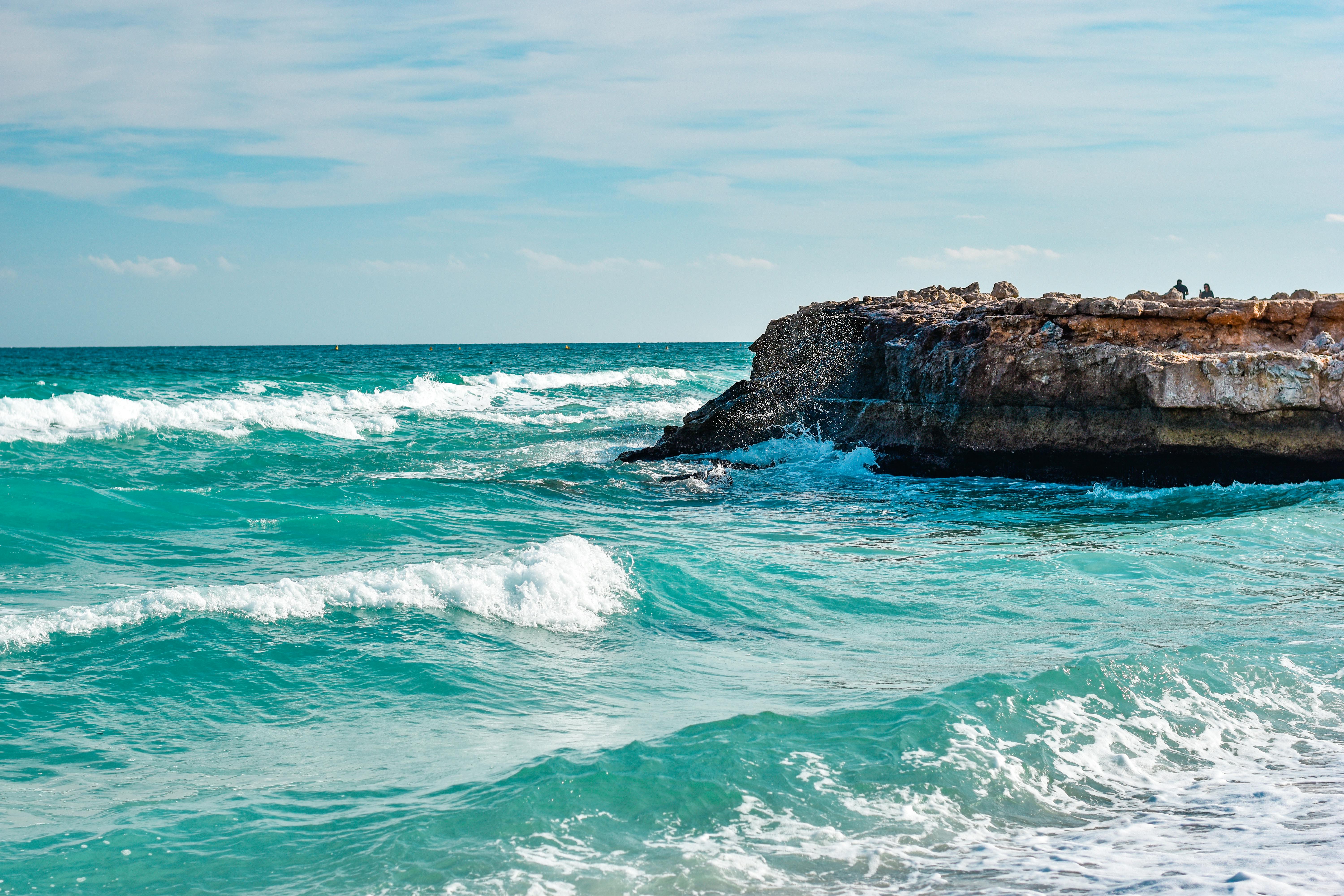 Des vagues océaniques vibrantes s'écrasant contre une falaise rocheuse sous un ciel bleu clair, mettant en valeur la beauté dynamique de la nature.