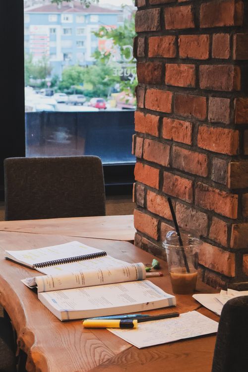 Free Inviting workspace with books, coffee, and rustic brick wall in a lively café setting. Stock Photo