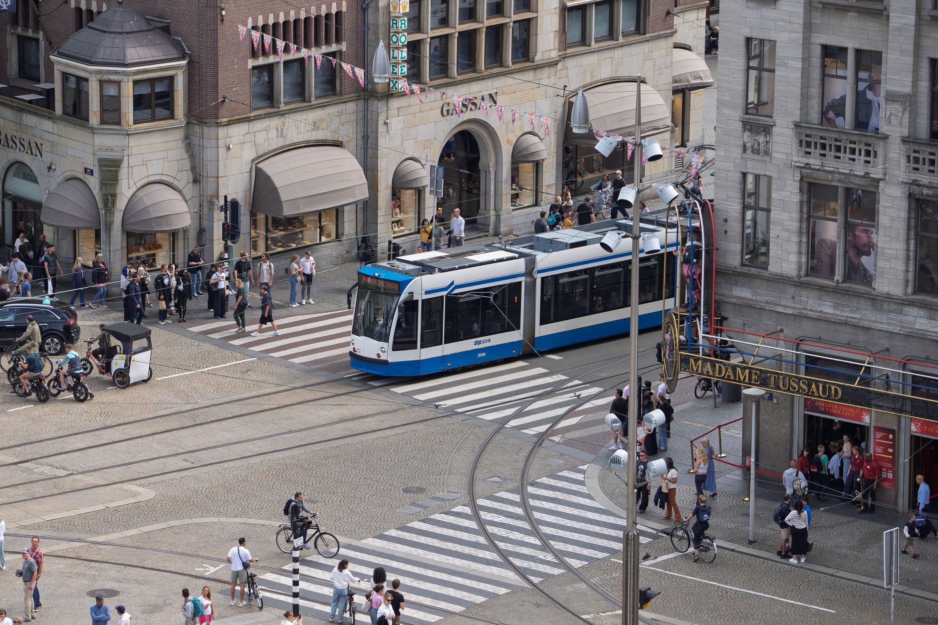 A bustling Amsterdam street with a tram and pedestrians, captured from above.