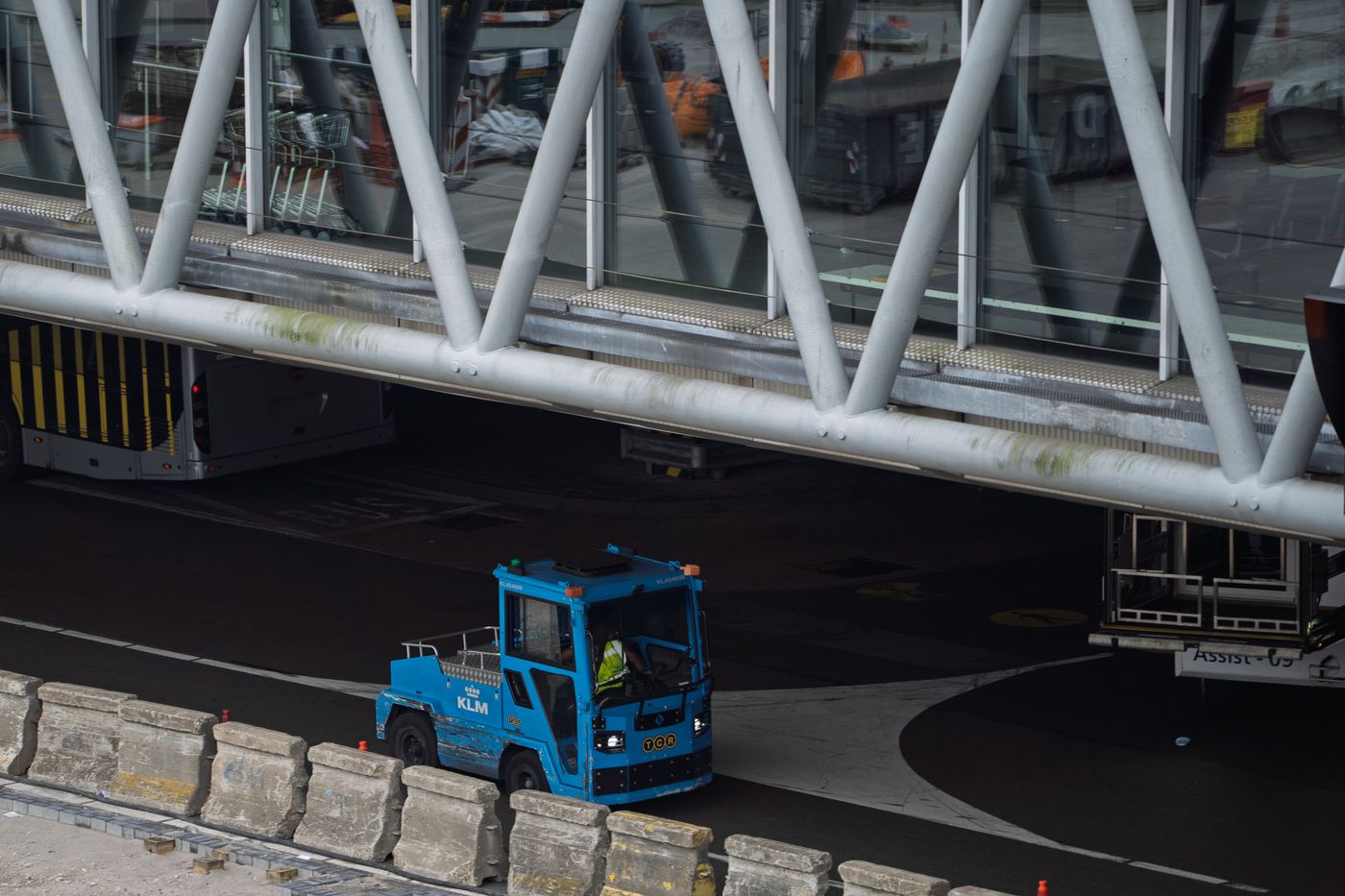A blue ground support vehicle moving beneath a jet bridge at a busy airport terminal