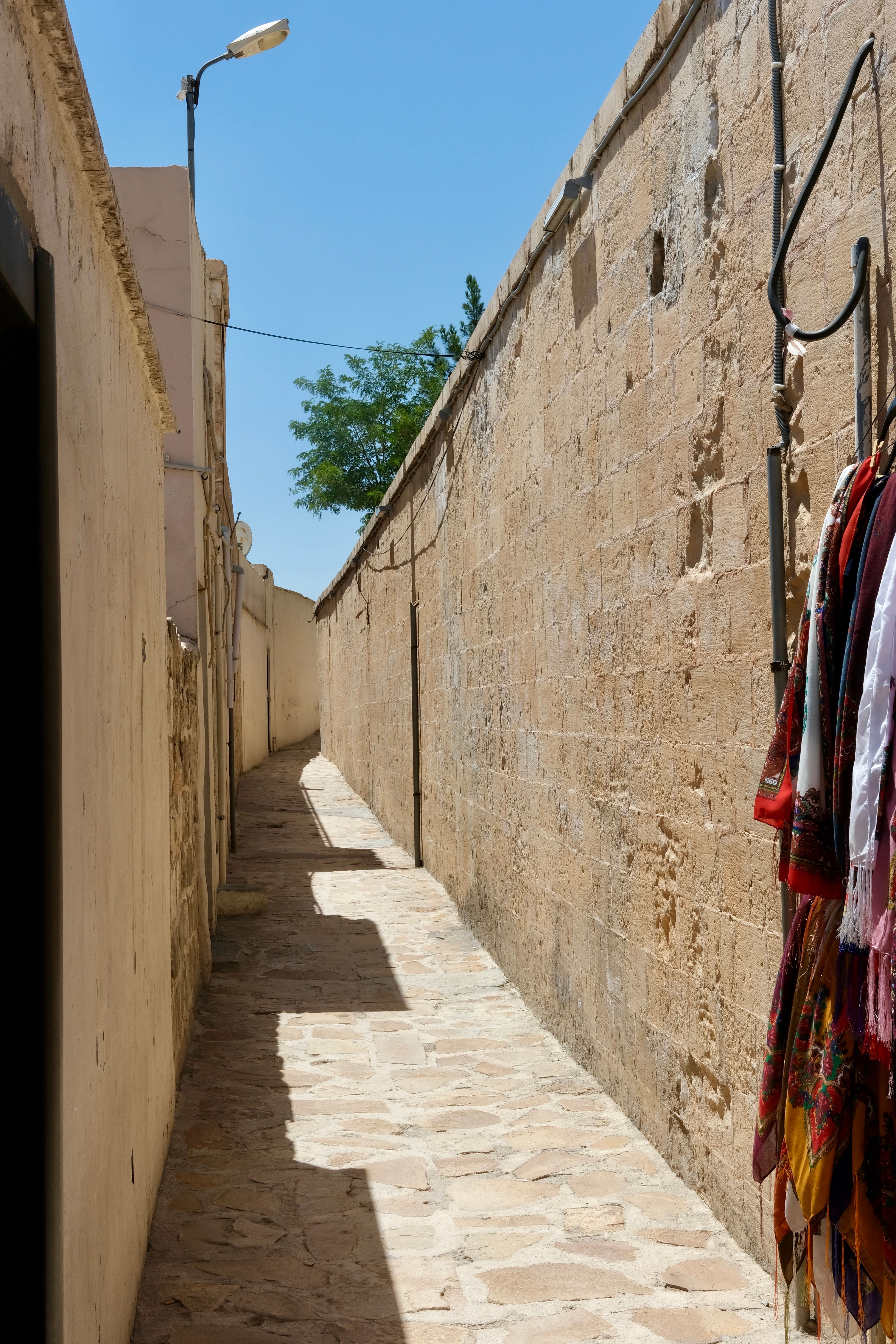 A sunlit stone alleyway with colorful fabrics hanging, evoking a Mediterranean vibe.