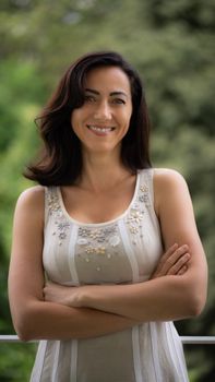 Elegant woman smiling with arms crossed in a serene outdoor setting in Milan, Italy.