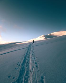 A hiker makes tracks in the fresh snow of Troms, Norway, under a clear winter sky.
