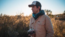 在一个阳光明媚的日子，男子身着休闲装，拿着模拟相机站在户外