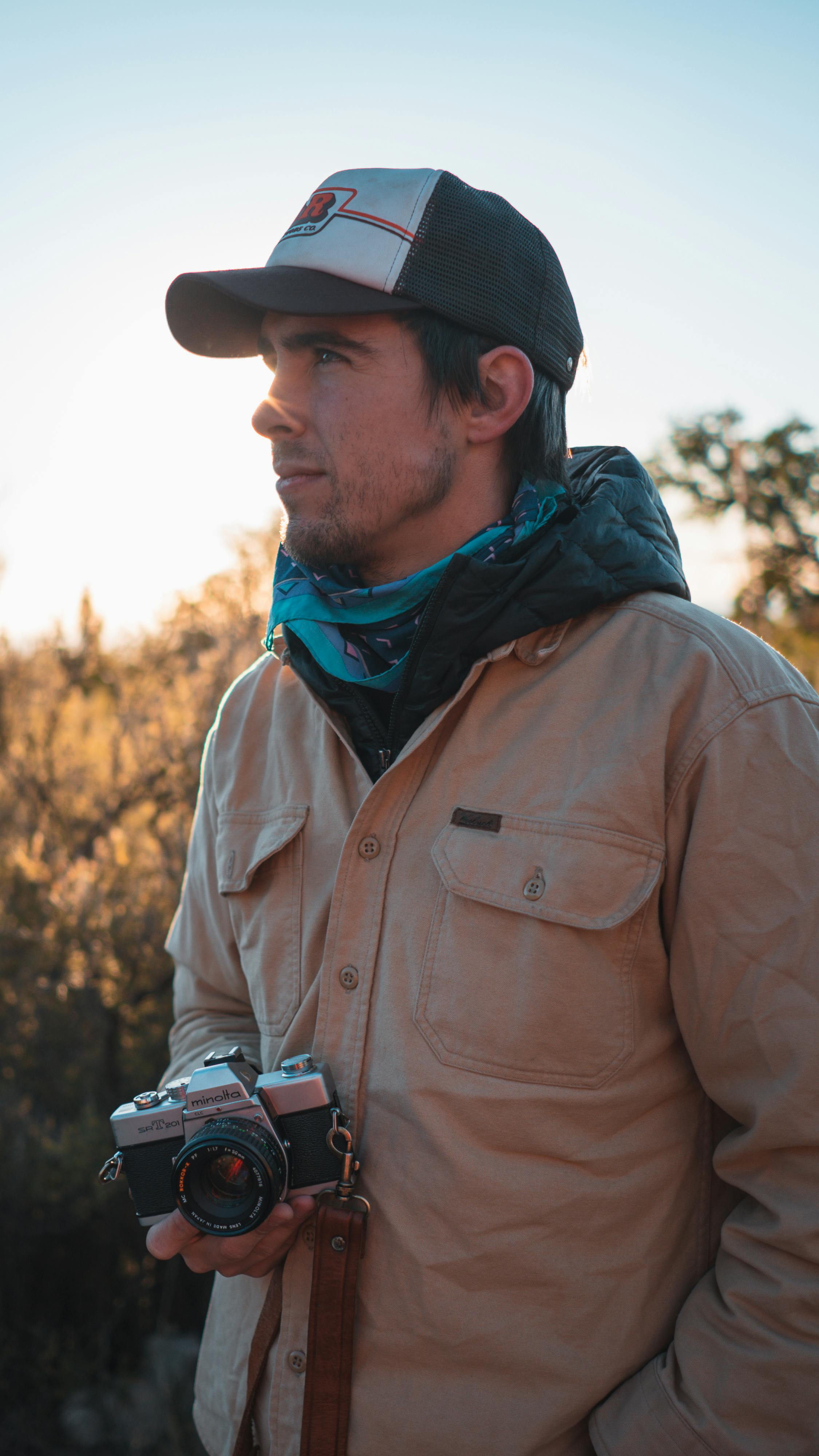 Man In Brown Jacket Facing Sideways Holding Black And Silver Dslr
