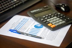 Desk with calculator, financial report, and pen, suggesting business analysis.