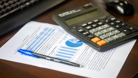 Desk with calculator, financial report, and pen, suggesting business analysis.