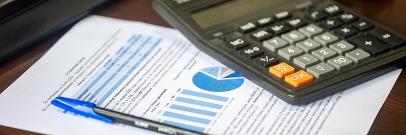 Desk with calculator, financial report, and pen, suggesting business analysis.