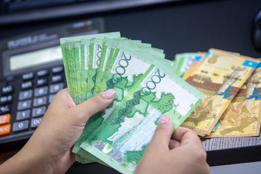 Close-up of hands counting Kazakhstani Tenge notes on a desk with calculator.