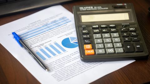 Close-up of a calculator, pen, and financial report on a wooden desk.