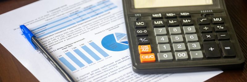 Close-up of a calculator, pen, and financial report on a wooden desk.
