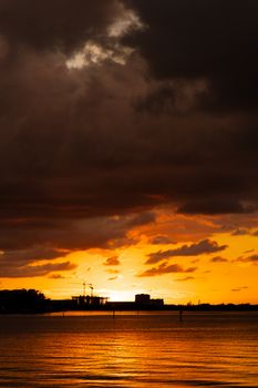 Stunning sunset with vibrant orange sky and dark clouds over a tranquil water body.