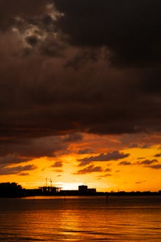 Breathtaking sunset view with vibrant orange skies reflecting on quiet waters under dramatic clouds.