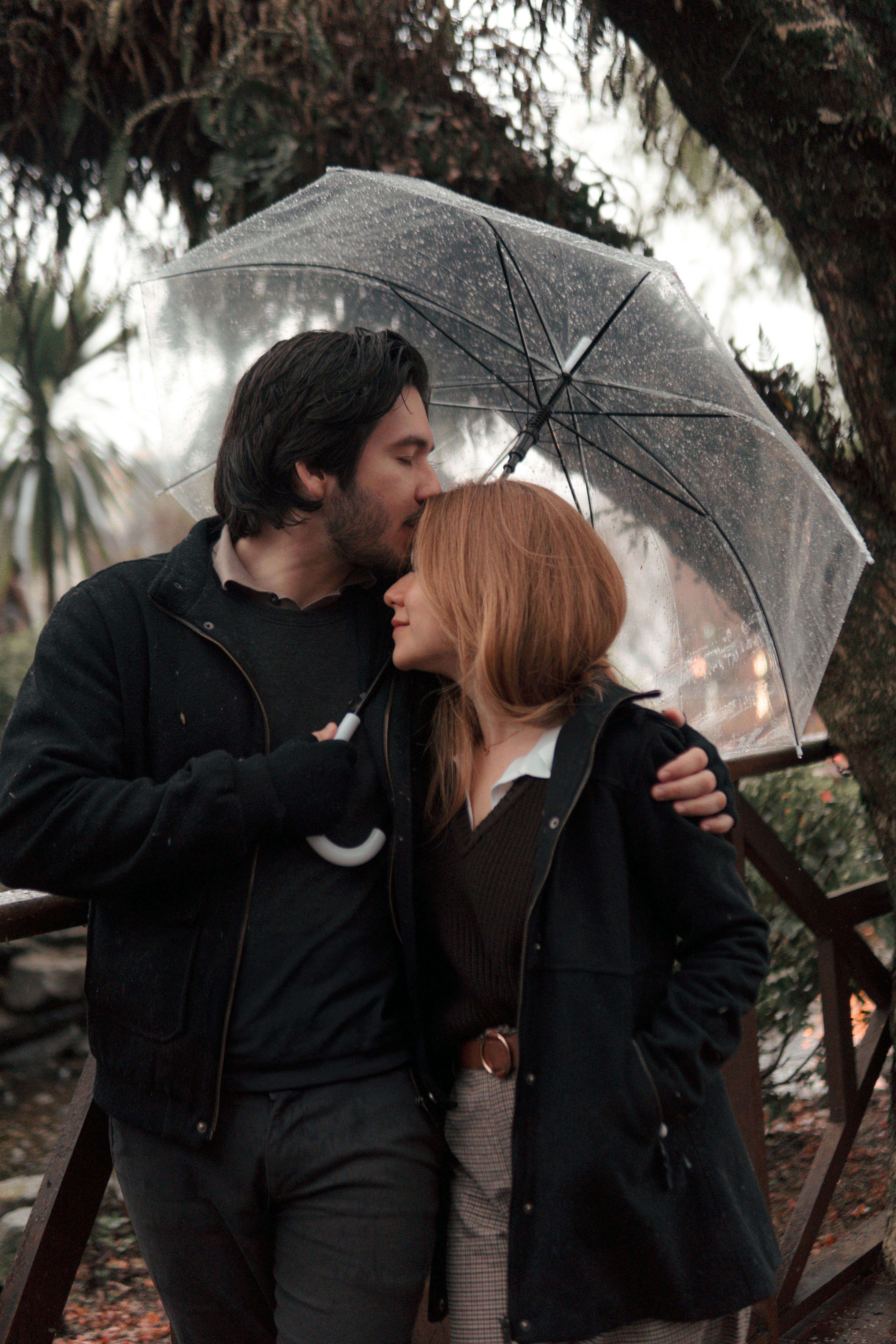Romantic couple embrace under a rainy umbrella in Gramado, Brazil, exuding warmth and love.