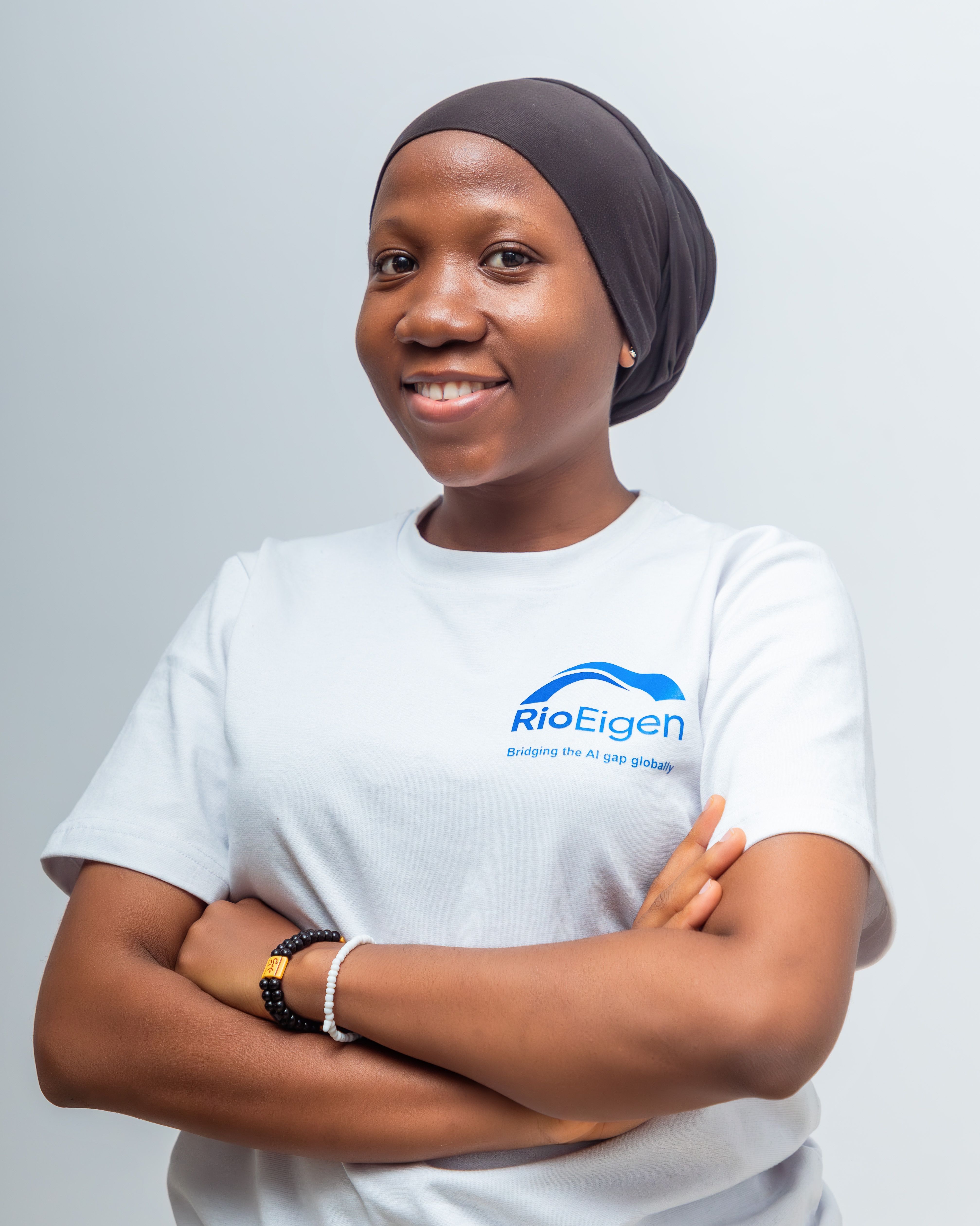 Portrait of a smiling woman wearing a RioEigen logo t-shirt, arms crossed.