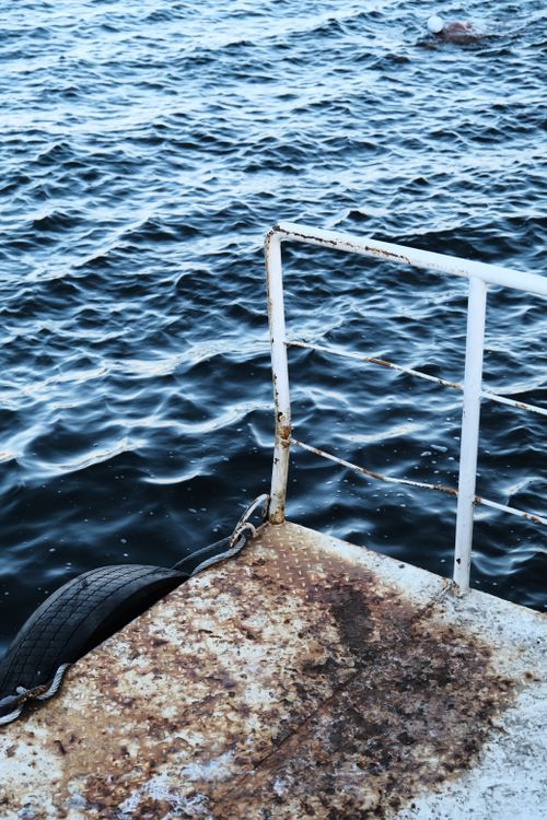 Free A rustic metal dock with railings and tire bumpers against a choppy blue sea background. Stock Photo