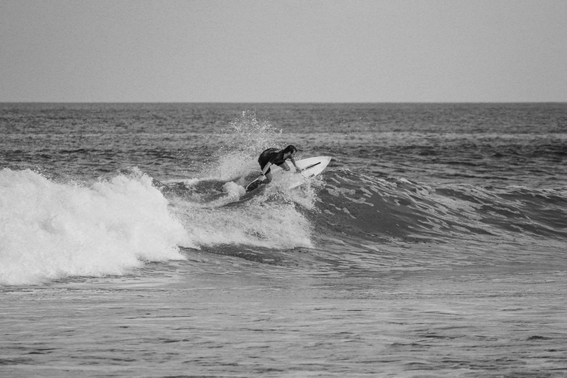 A surfer skillfully rides a wave at a Bali beach, captured in striking black and white.