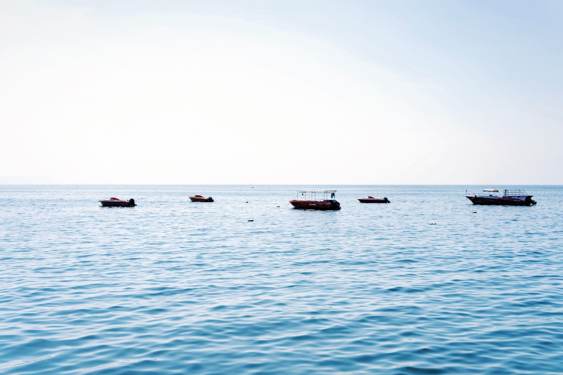 Tranquil seascape featuring small boats floating on calm waters under a bright sky.
