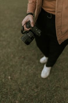 A person casually holds a DSLR camera while standing on grass, showcasing casual outdoor photography.
