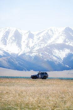 A rugged SUV exploring open grasslands beneath majestic snowy mountains, ideal for adventure travel.