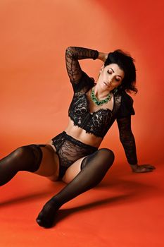 Woman in lace lingerie posing elegantly against a vibrant orange backdrop. Fashion and style.