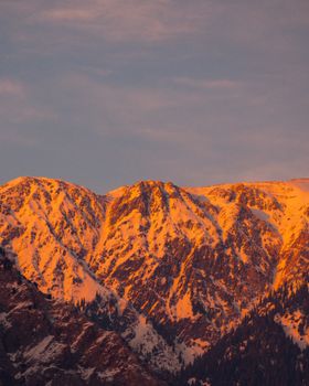 Stunning view of snow-capped mountains bathed in golden hour hues under a vibrant sky.
