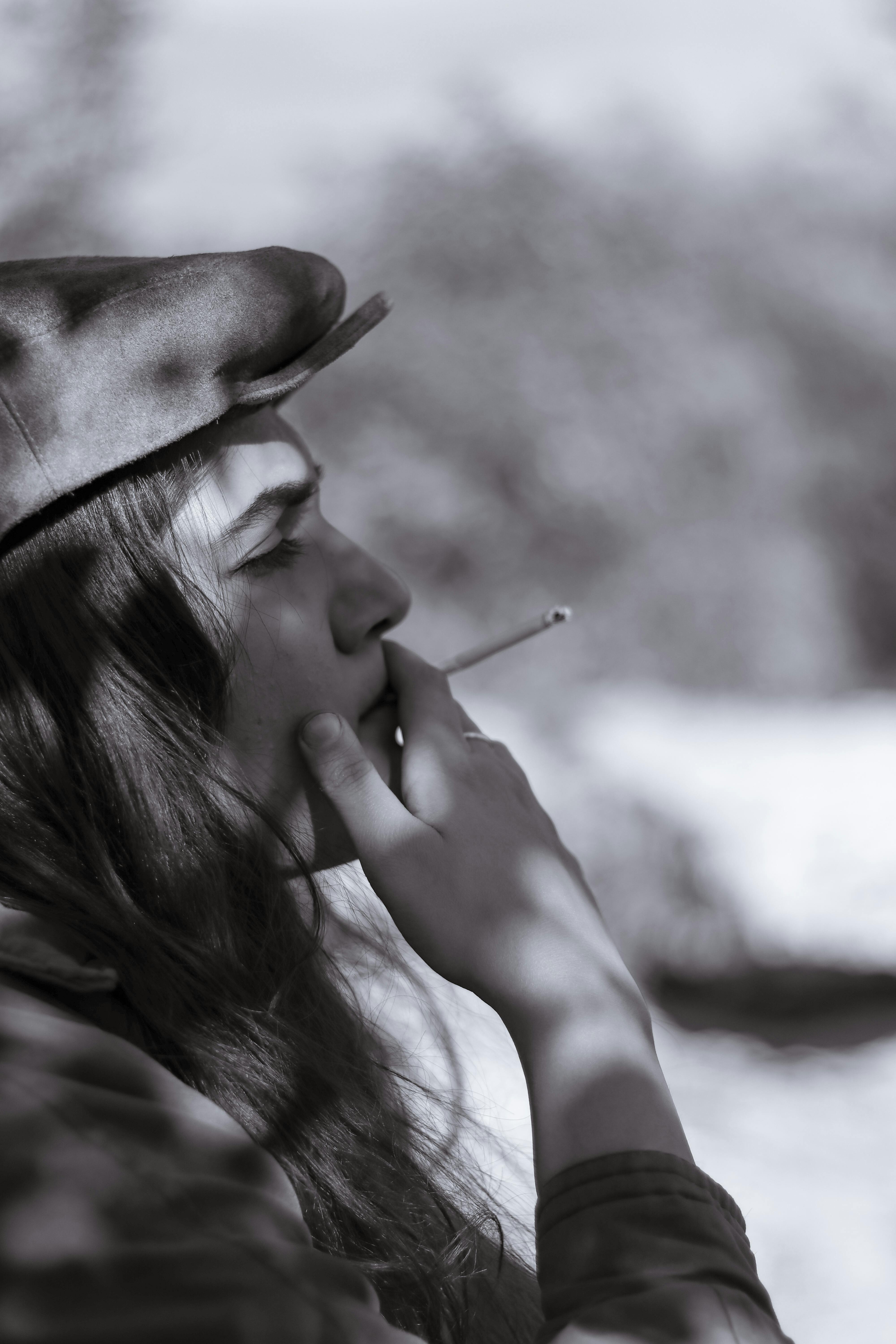 Artistic black and white portrait of a woman smoking, captured outdoors in a serene setting.