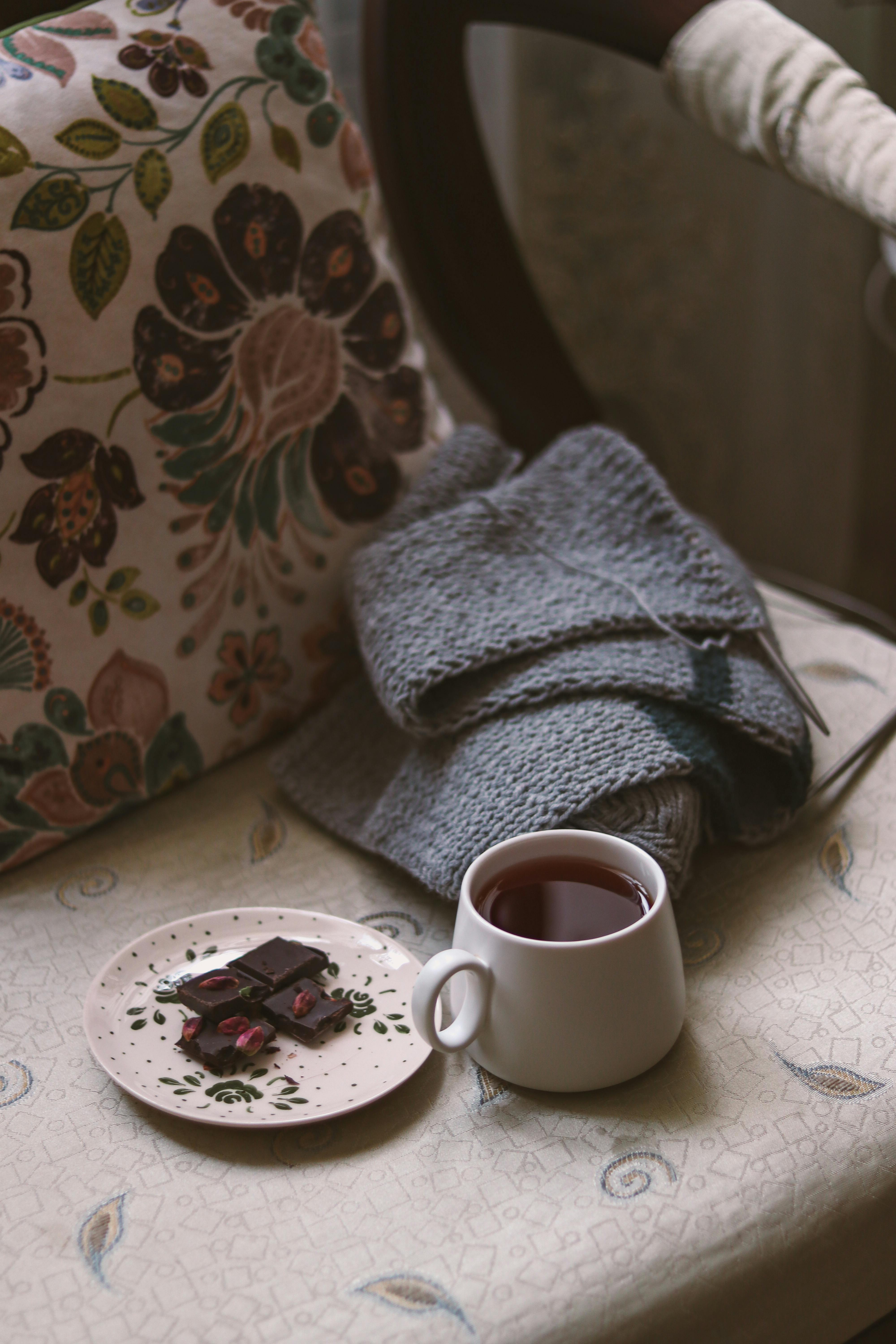 Warm, cozy scene with a knitting project, a cup of tea, and chocolate on a vintage chair.