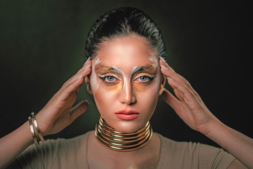 Free Close-up portrait of a woman with creative gold makeup and jewelry, conveying elegance and modern artistry. Stock Photo