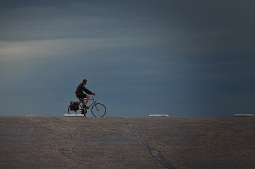Free A lone cyclist rides under moody skies on a coastal road in Ouddorp, Netherlands. Stock Photo