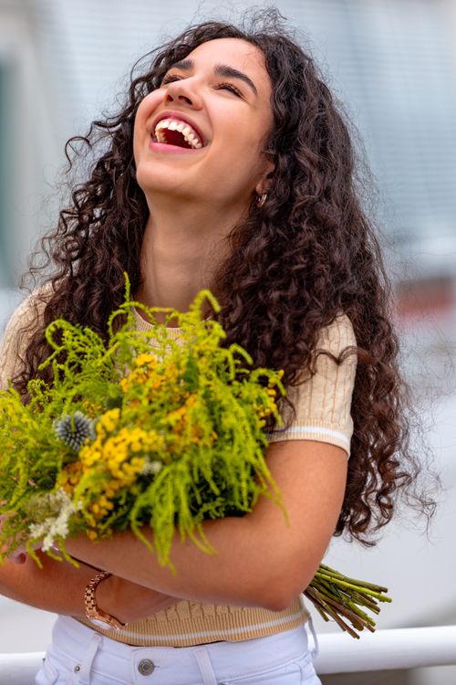 Free Young woman with curly hair joyfully holding a colorful bouquet of flowers. Stock Photo
