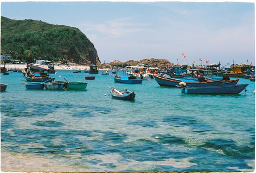 Colorful fishing boats anchored in the clear turquoise waters near a rocky coastline.