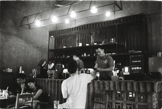 A candid black and white scene inside a coffee shop with patrons and baristas.