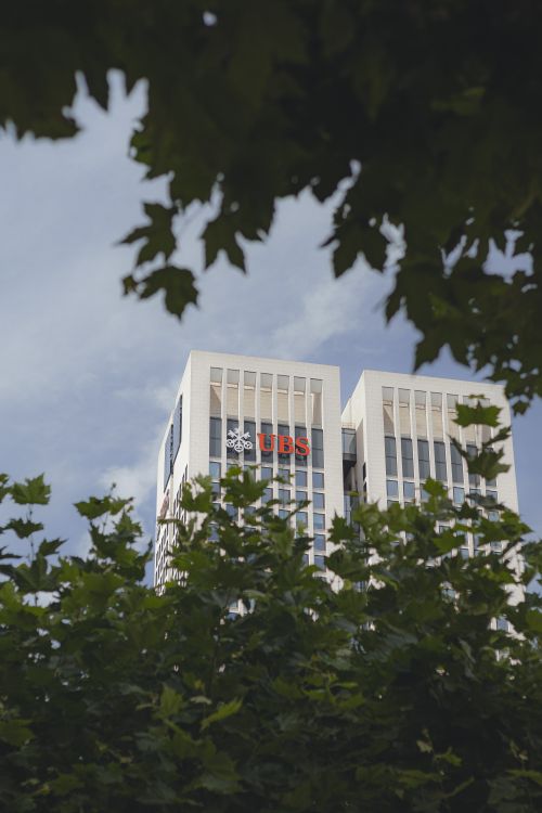 Free A UBS skyscraper framed by green leaves against a clear sky. Stock Photo