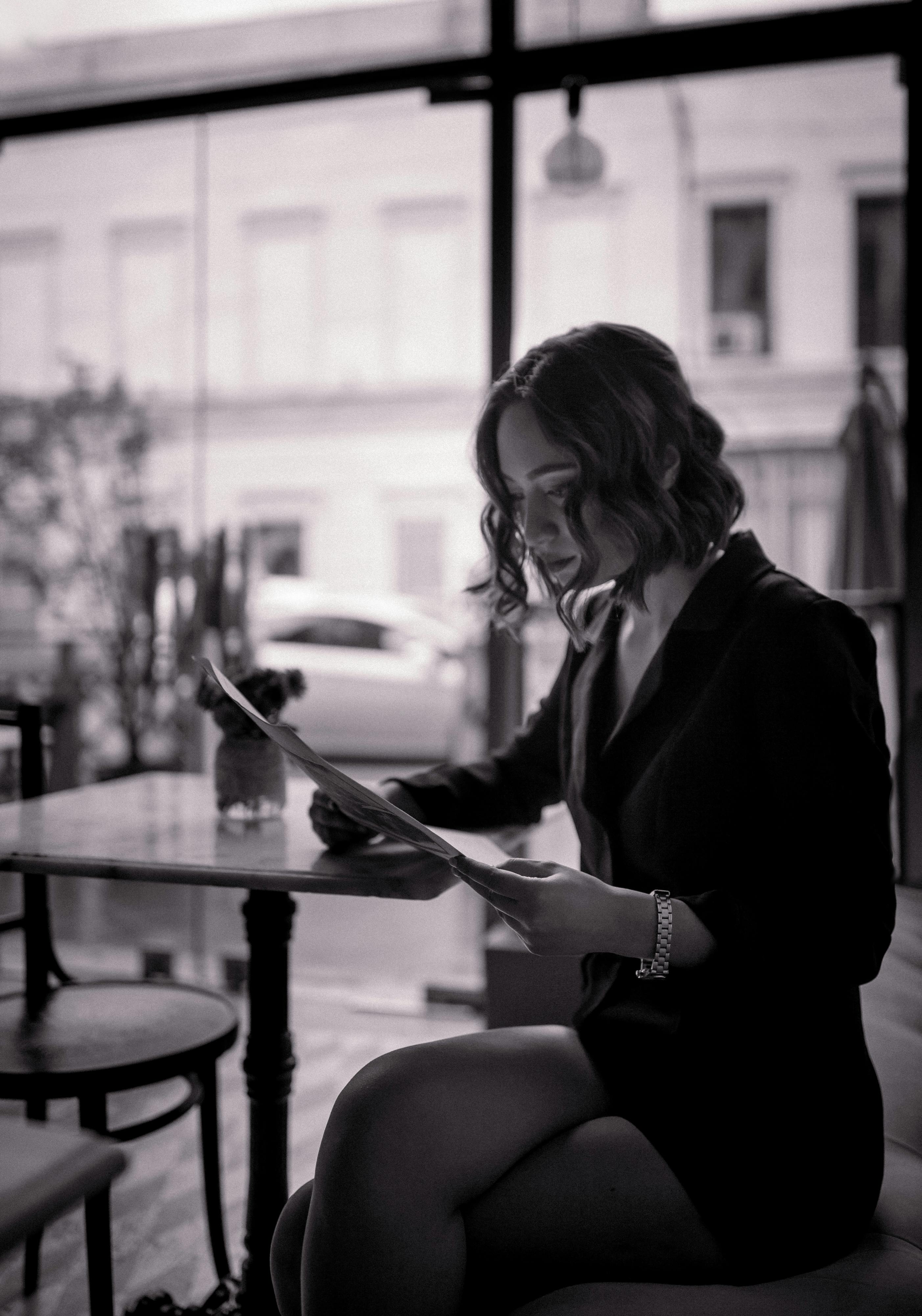 Gratis Retrato monocromático de una mujer leyendo en un café elegante, que irradia un estado de ánimo sofisticado. Foto de stock