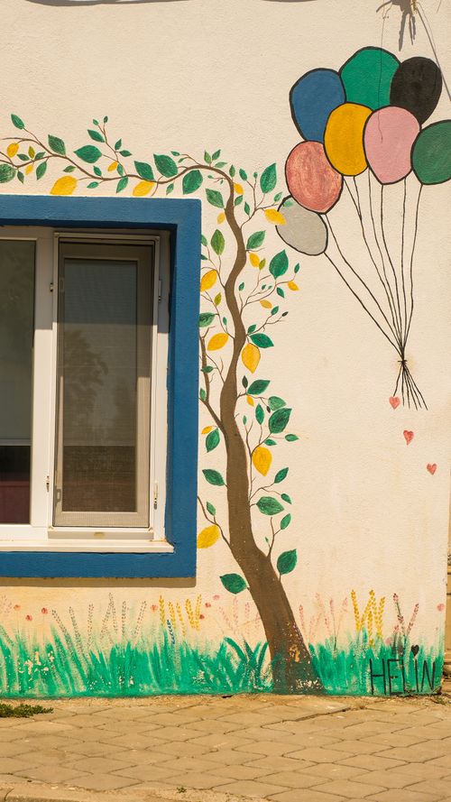 Free Vibrant mural of a tree and balloons on a building wall with a window Stock Photo