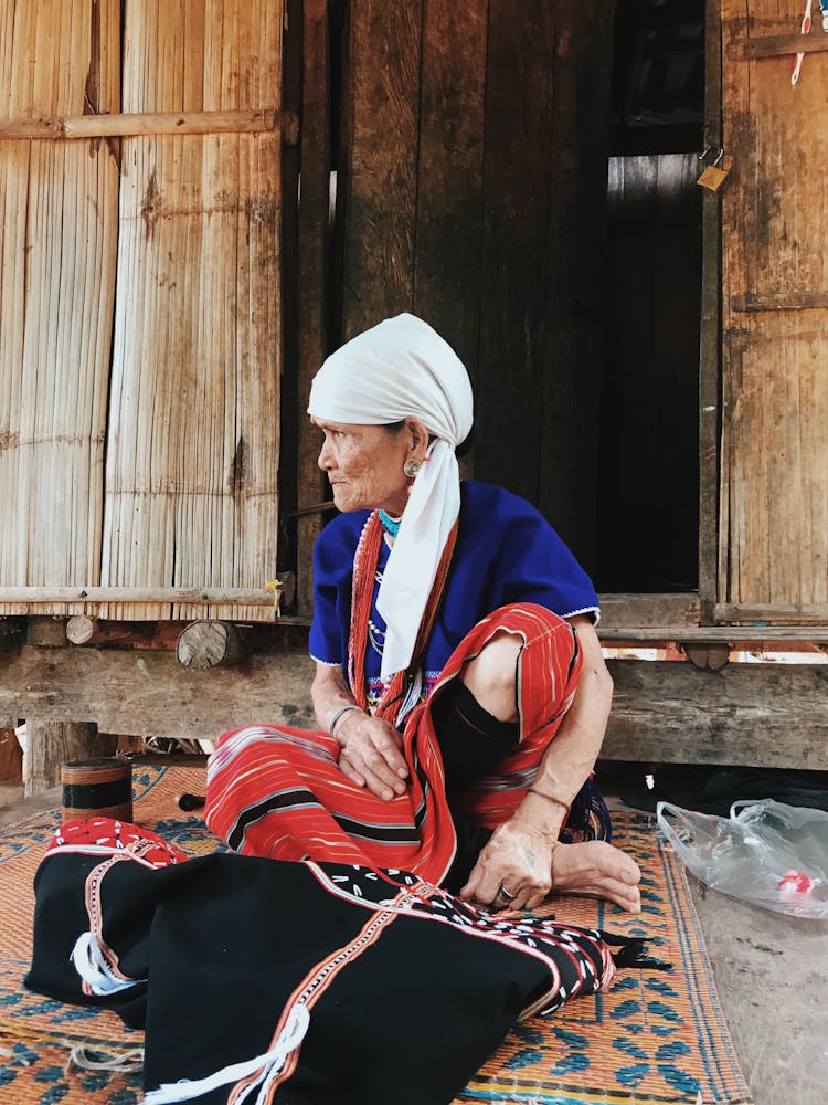 Mature Ethnic Woman Sitting On Carpet On Street