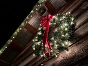 一个点燃的圣诞花环特写镜头，上面挂着红色蝴蝶结，悬挂在质朴的木谷仓上，展现了节日装饰