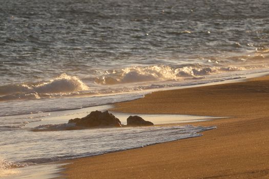 Golden hues of a sunset cast over a serene beach with gentle waves.