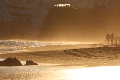 Free Silhouetted figures walk along a golden sandy beach during sunset, creating a serene and warm atmosphere. Stock Photo