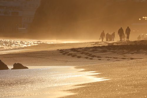 Free Golden sunset on the beach with silhouettes of people, creating a serene and warm atmosphere. Stock Photo