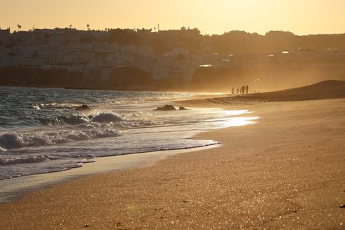 Free A tranquil beach scene during sunset with silhouetted figures in the distance and a golden glow. Stock Photo