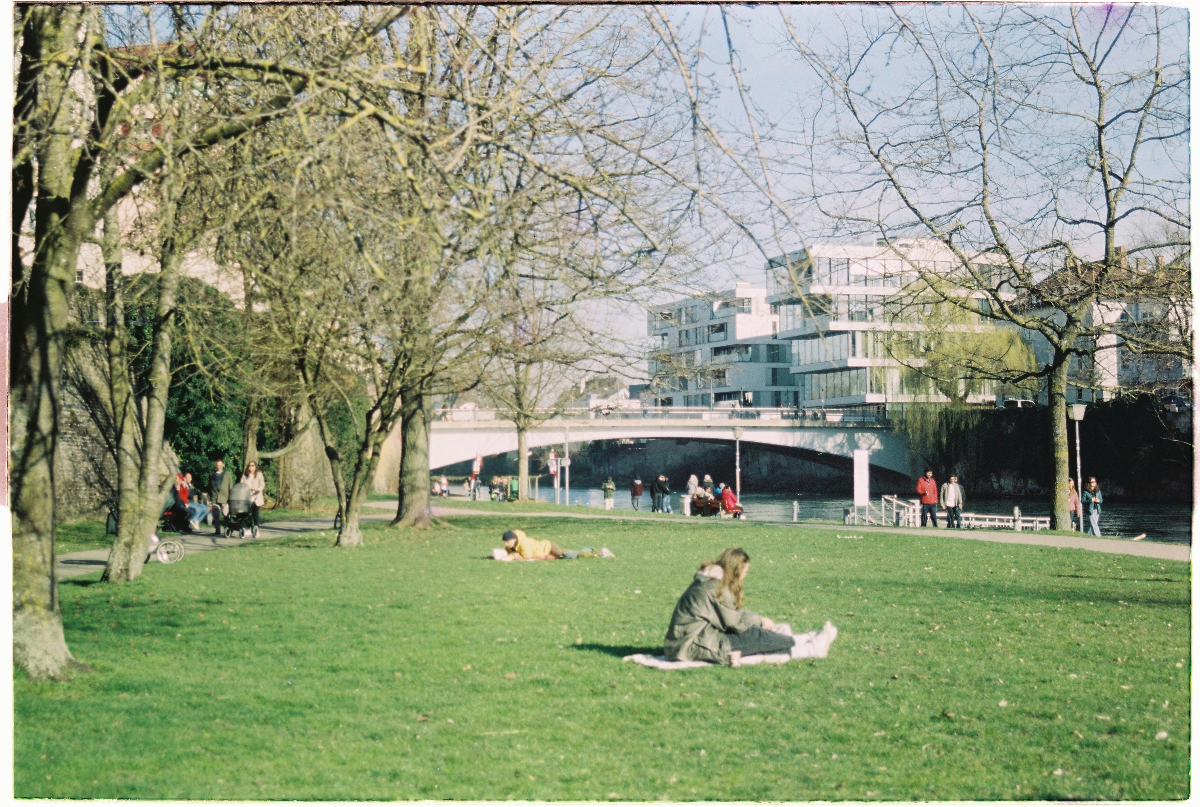 People enjoying a sunny day in a park by the river in Ulm, Germany.