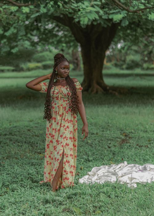Free Elegant woman in a floral dress poses under a big tree in a lush green park. Stock Photo
