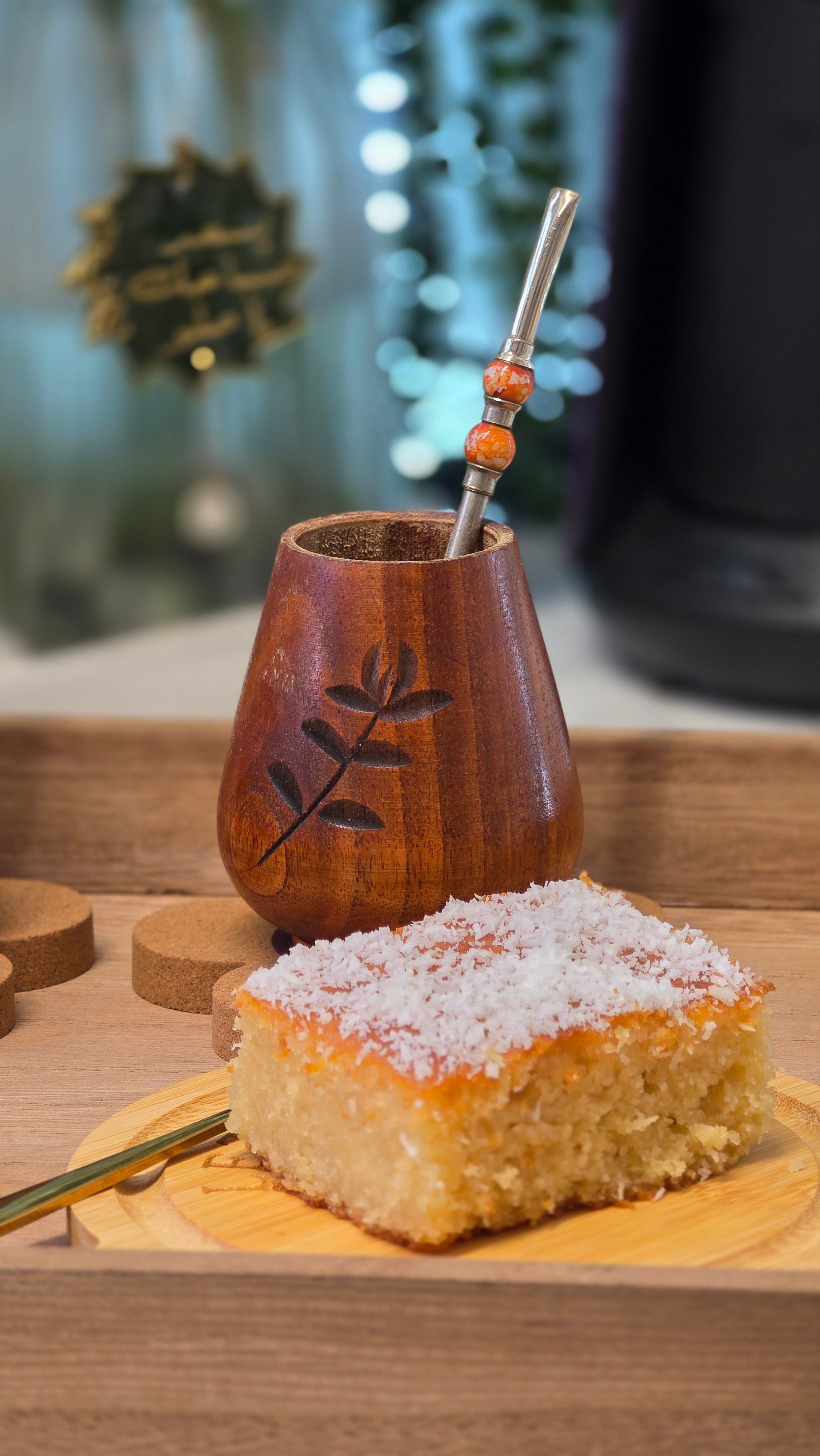 Wooden yerba mate gourd with straw and coconut cake on tray.