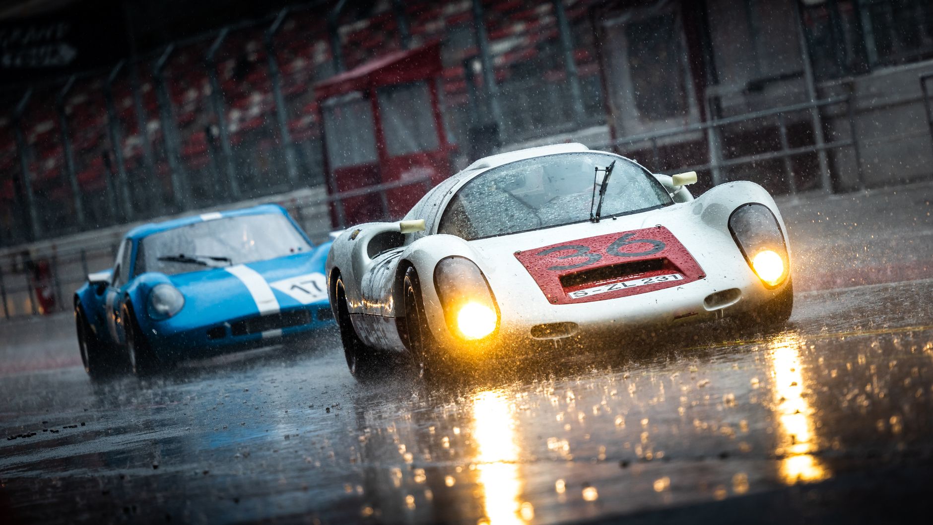 Classic sports cars racing in wet conditions, showcasing speed and style.